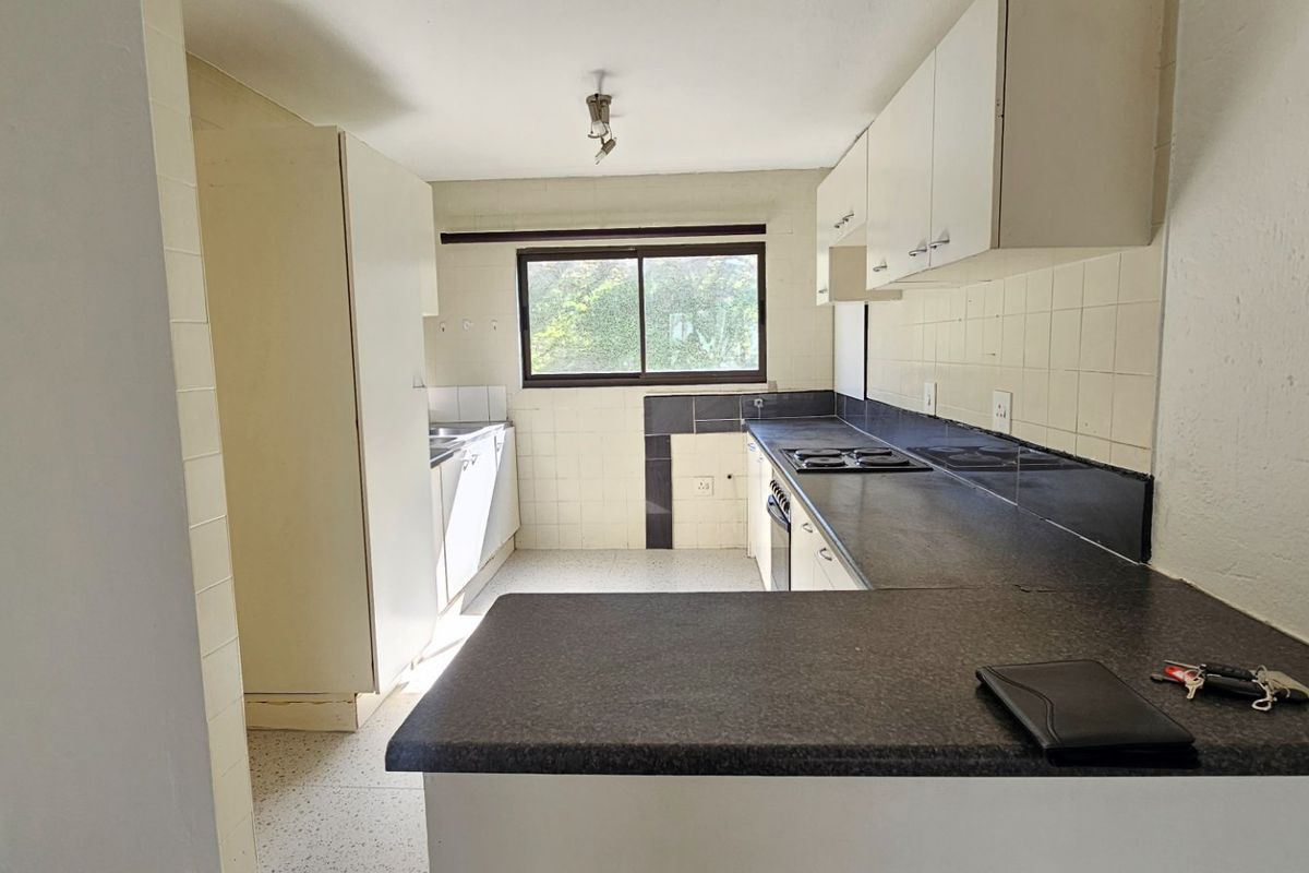 A functional, empty kitchen featuring built-in cabinetry, dark laminate countertops, a built-in hob and oven, and tiled finishes throughout.