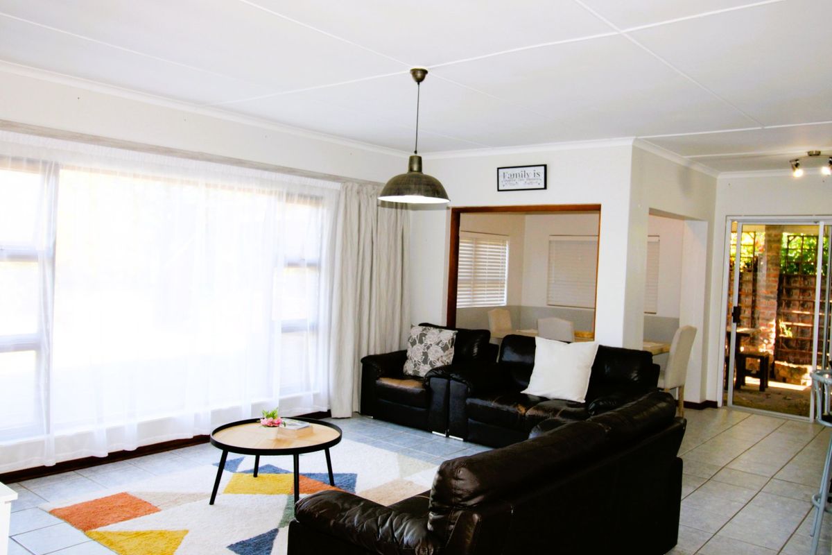 A bright living room featuring tiled flooring, a large window with natural light, and an open-plan layout connecting to adjacent living spaces.