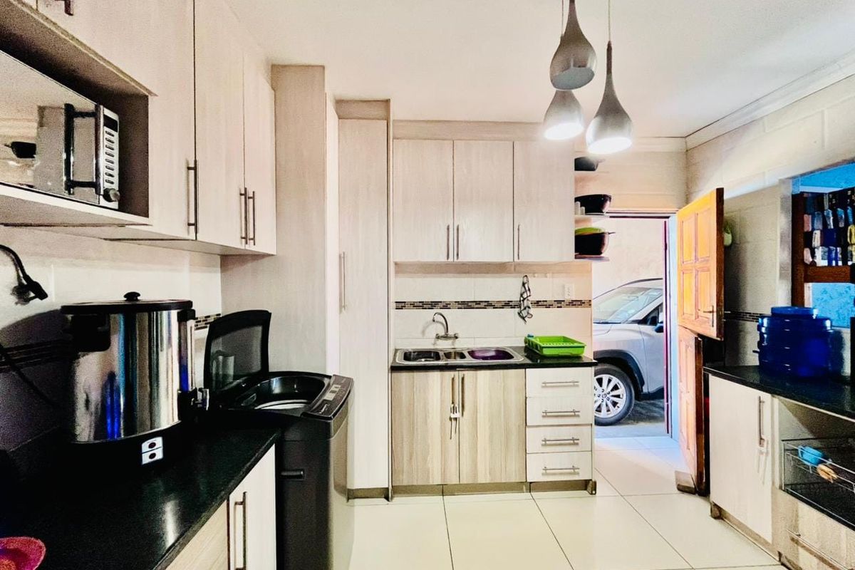 A functional kitchen featuring light wood-finish cabinetry, dark countertops, tiled flooring, and a double sink, with direct access to the exterior.
