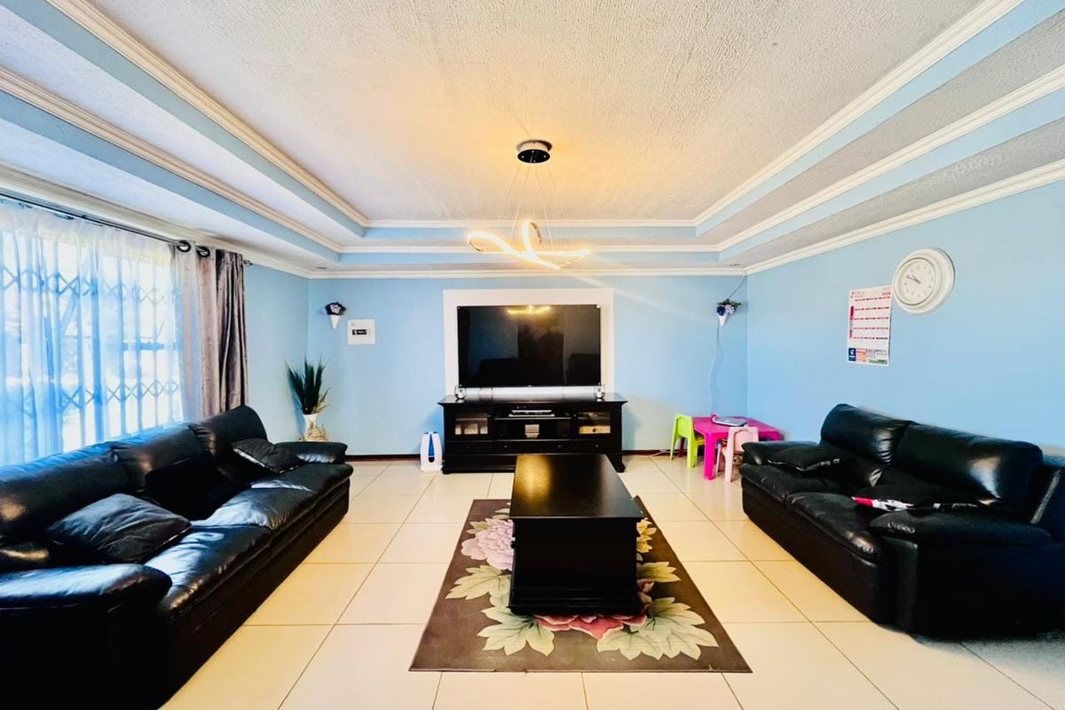 Spacious living room featuring a decorative tray ceiling, modern lighting, and neutral ceramic floor tiles, providing a comfortable and well-lit family area.