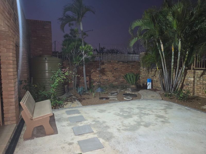 A private rear garden area featuring a concrete patio, established palm trees, a water storage tank, and secure brick boundary walls.