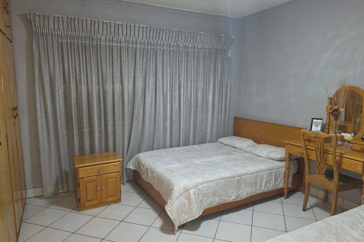 A bedroom featuring tiled flooring and built-in cupboards, offering a functional space with neutral wall tones.