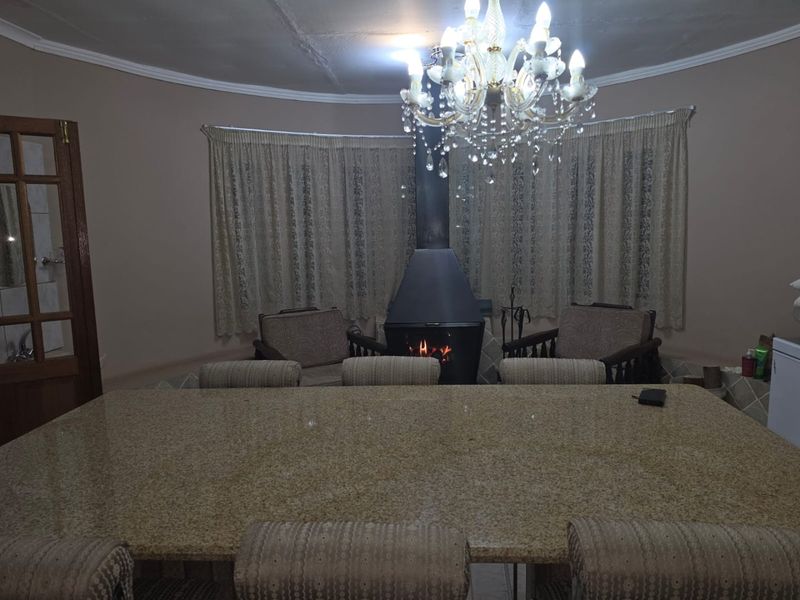 A living area featuring a central freestanding fireplace, a large granite-topped island, and a decorative crystal chandelier under a coved ceiling.