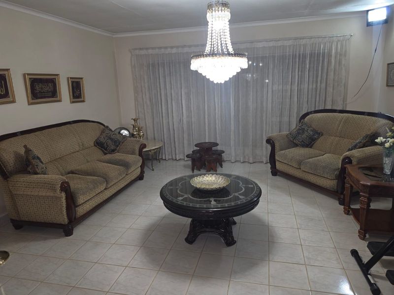 A spacious living room featuring tiled flooring and a prominent crystal chandelier, offering a neutral base for potential interior updates.