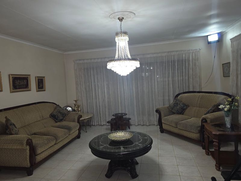 A traditional living room featuring tiled flooring, a central crystal chandelier with a decorative ceiling rose, and floor-to-ceiling window treatments.
