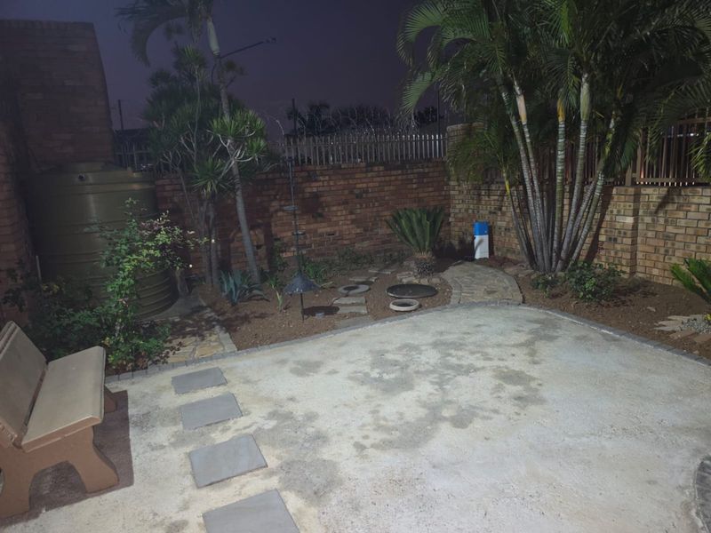 A rear garden area featuring a paved patio, brick boundary walls, and a water storage tank, captured during evening hours.