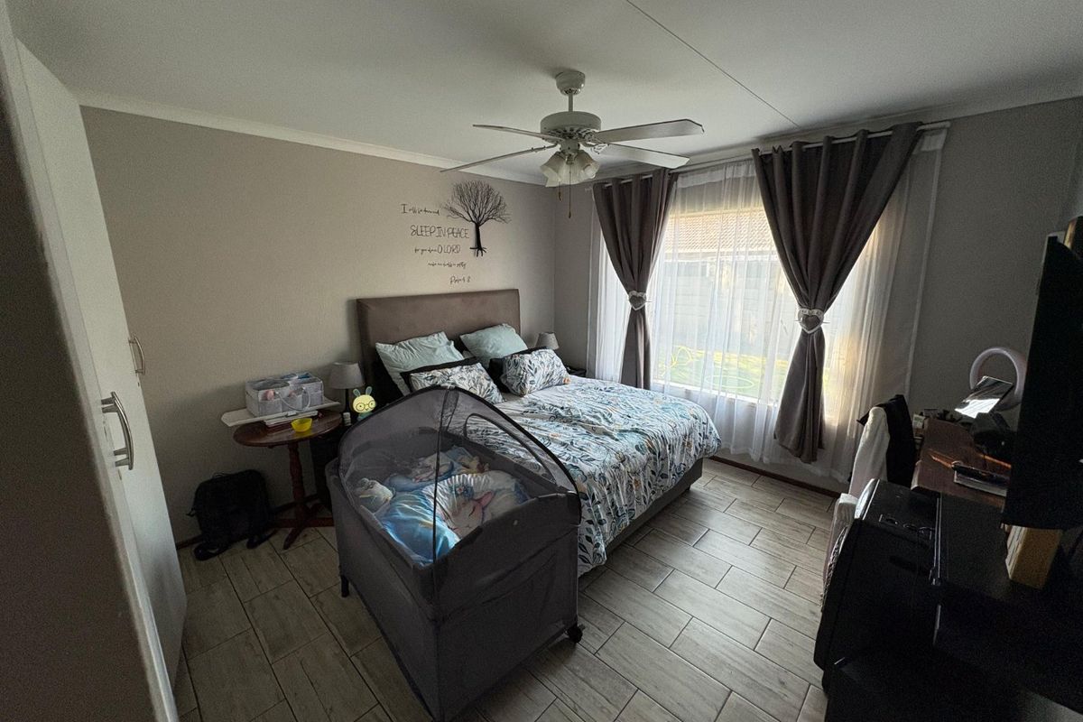 A functional bedroom featuring tiled flooring, a ceiling fan, and built-in wardrobe storage, offering a comfortable and practical living space.