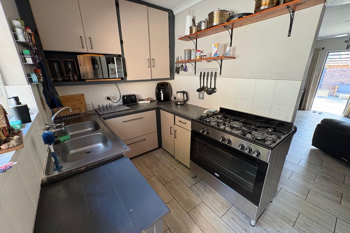 A functional kitchen featuring a gas stove, double sink, tiled backsplash, and ample built-in cabinetry with open shelving for storage.