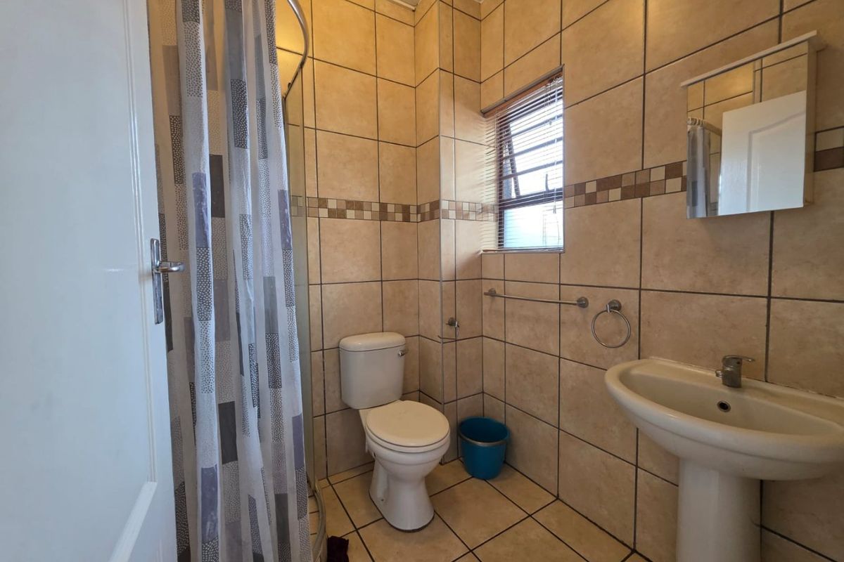A functional bathroom featuring a pedestal basin, toilet, and shower enclosure with neutral floor-to-ceiling wall tiling.