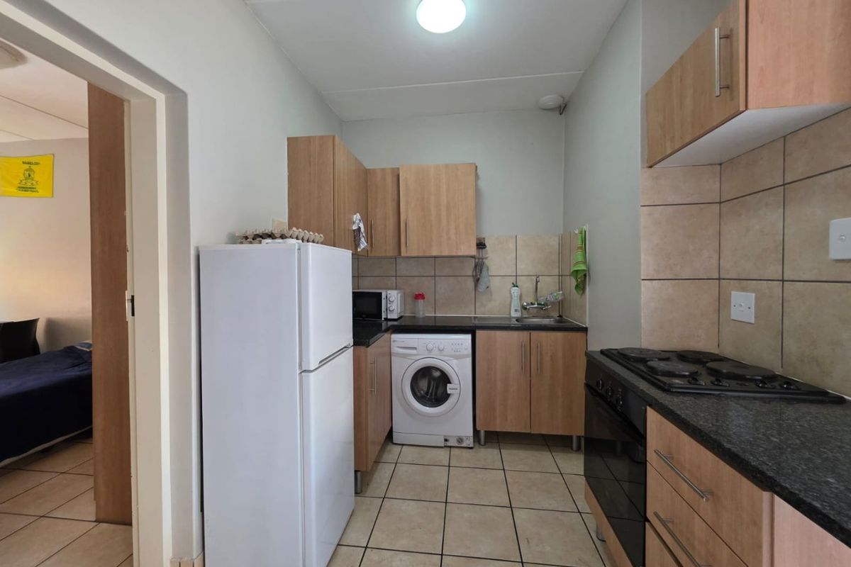 Compact kitchen featuring light wood cabinetry, granite countertops, tiled backsplash, and integrated oven with hob, with space for a washing machine.