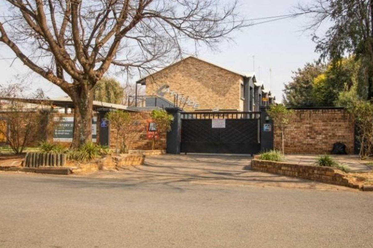 Front exterior view of the apartment complex featuring a brick boundary wall, secure metal gate, and paved entrance area.