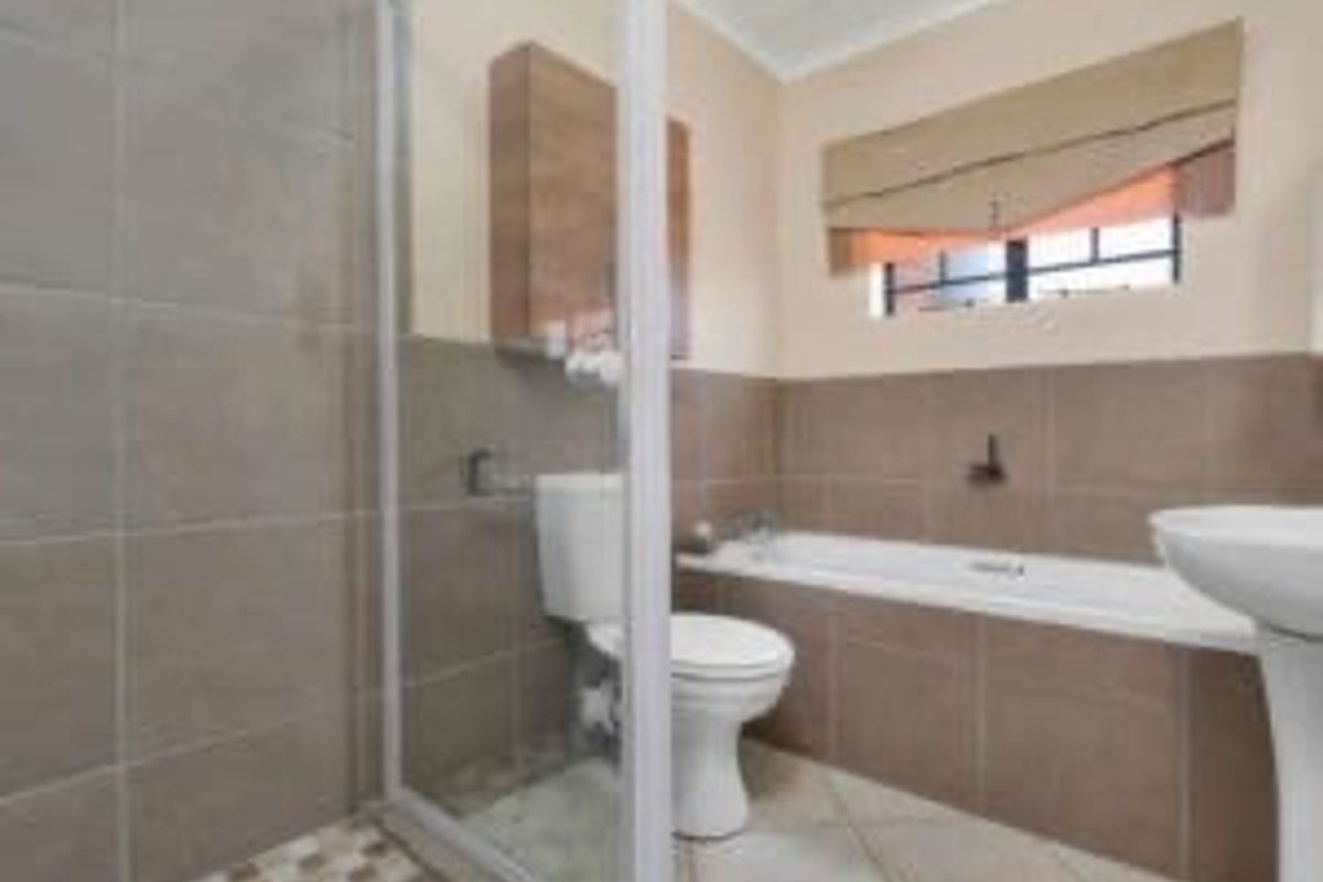 A functional bathroom featuring a shower enclosure, bathtub, pedestal basin, and toilet with neutral wall and floor tiling.