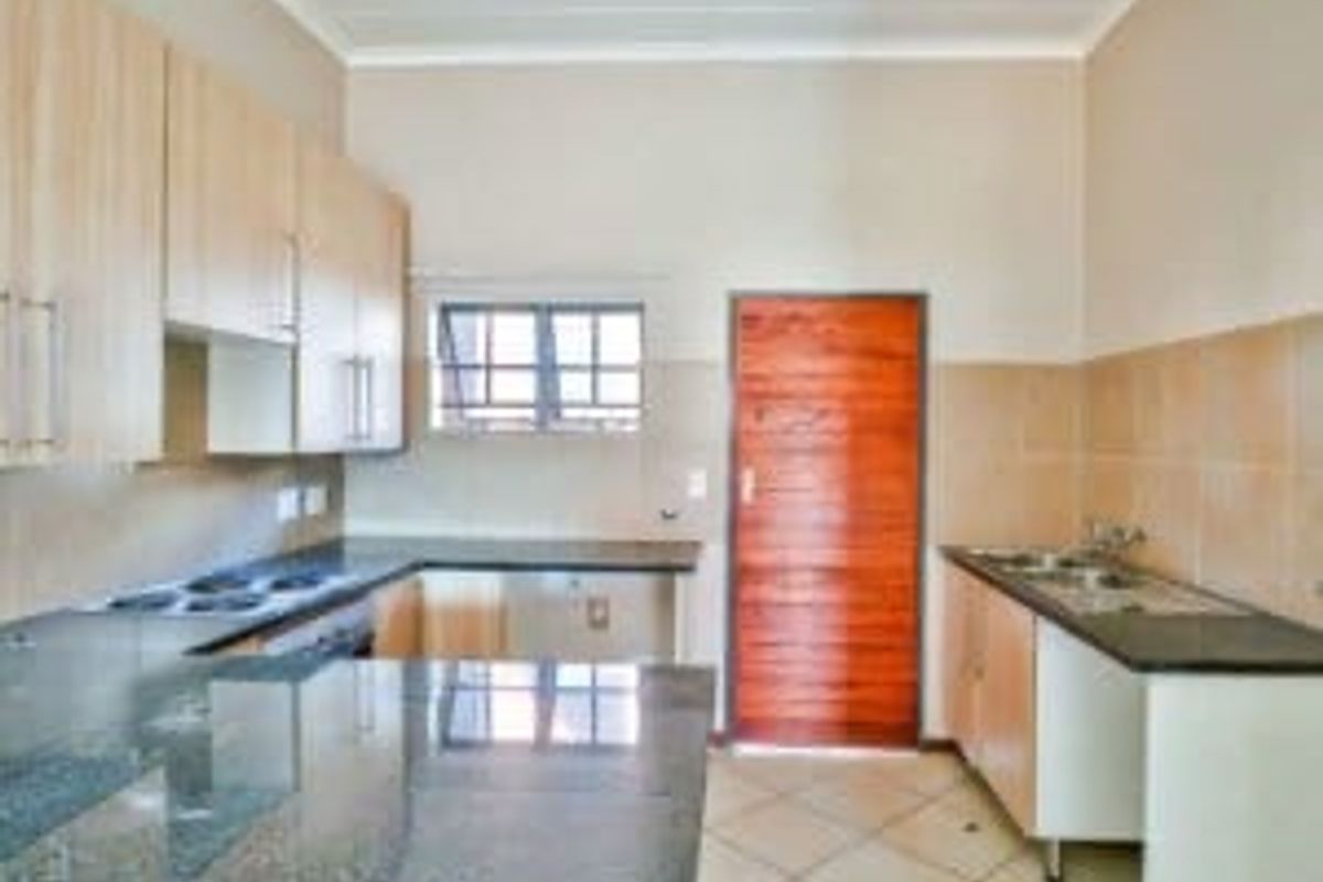 A functional kitchen featuring granite countertops, built-in cabinetry, a stainless steel sink, and tiled flooring, offering a clean and practical workspace.