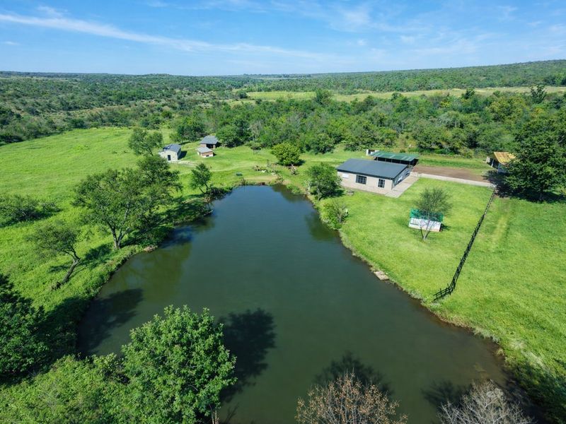 Aerial view of a rural farm property featuring a large dam, open grazing land, and multiple outbuildings set within a natural landscape.