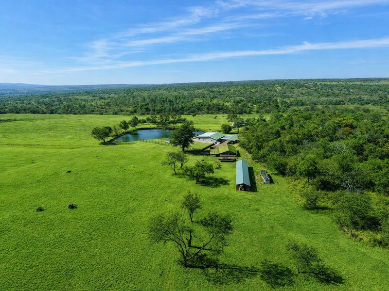 Aerial view of a sprawling farm property featuring multiple outbuildings, a private dam, and extensive green pasture land.