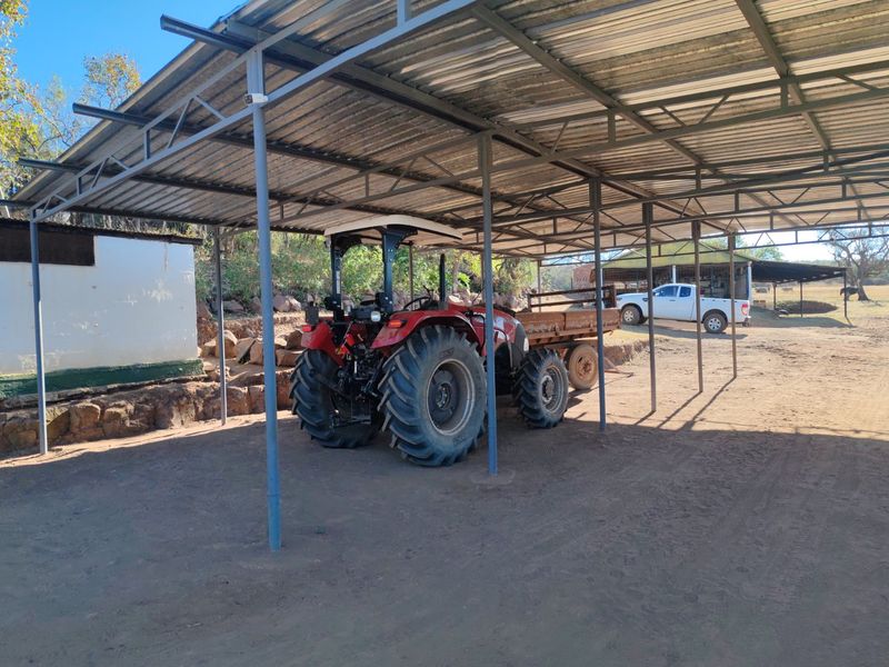 A functional open-sided farm utility shed featuring a corrugated metal roof supported by a steel frame, providing covered storage for farm equipment.