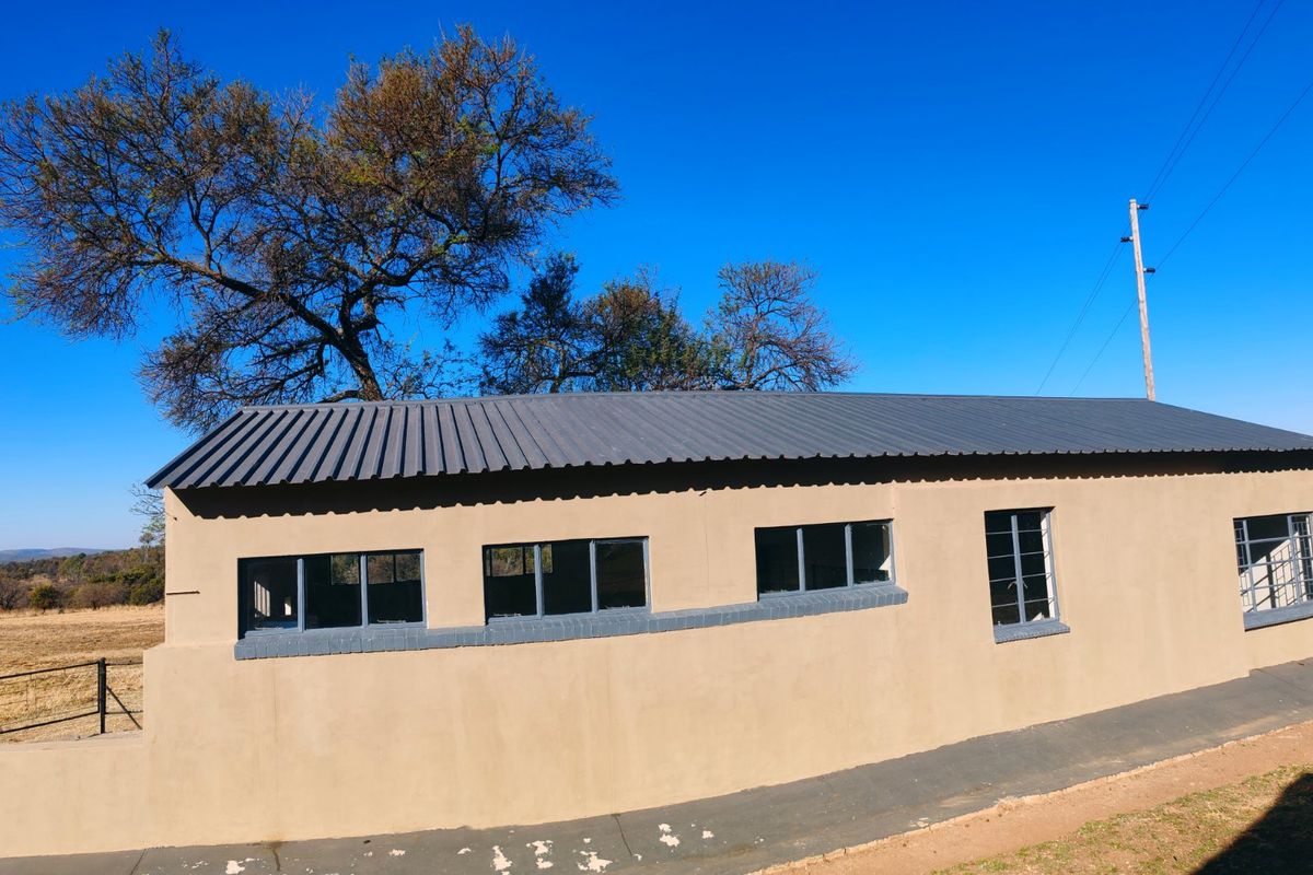 A side view of a farm outbuilding featuring a corrugated metal roof, steel-framed windows, and a concrete apron set against a rural landscape.