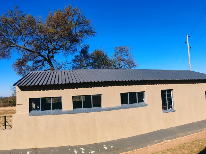 A side view of a farm outbuilding featuring a corrugated metal roof, steel-framed windows, and a concrete apron set against a rural landscape.