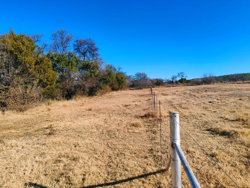 An expansive open field on the farm property, featuring established wire fencing and natural vegetation under a clear blue sky.