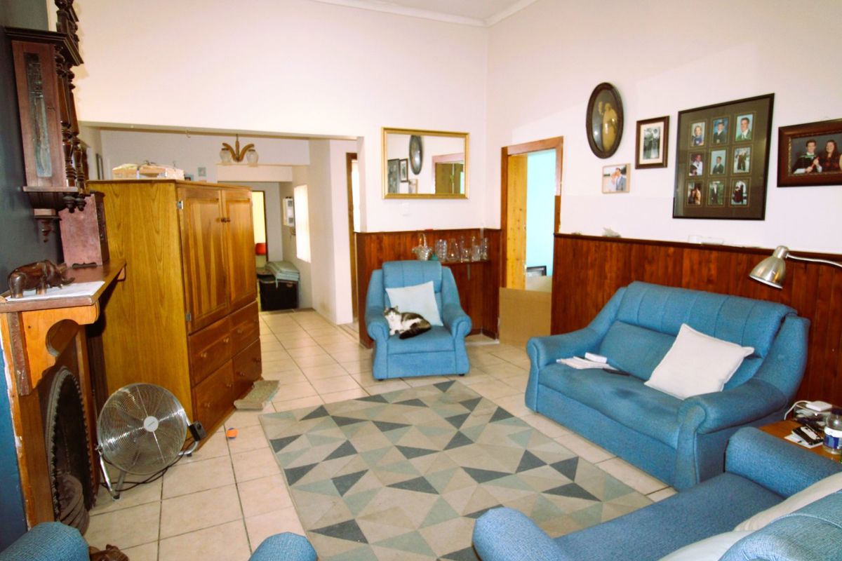 A living room featuring tiled flooring, timber wall paneling, and a traditional fireplace surround, leading into an adjacent hallway area.