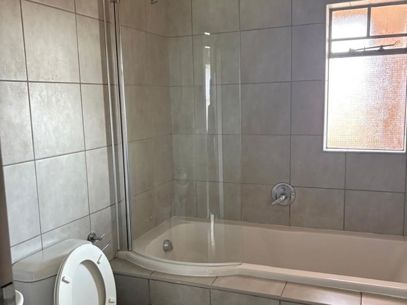 A functional bathroom featuring a bathtub with a glass shower screen, tiled walls, and a standard toilet.