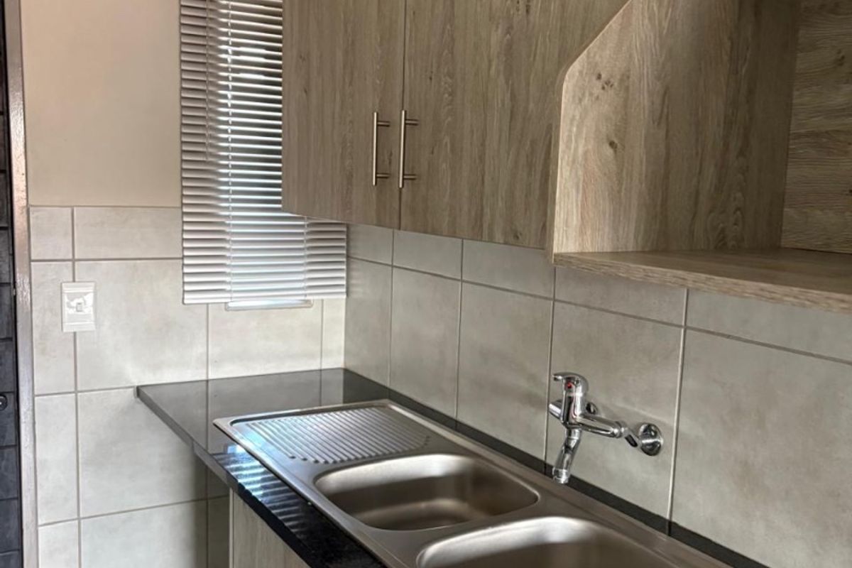 A clean and functional kitchen area featuring modern wood-look cabinetry, dark granite countertops, and a double stainless steel sink with tiled splashbacks.