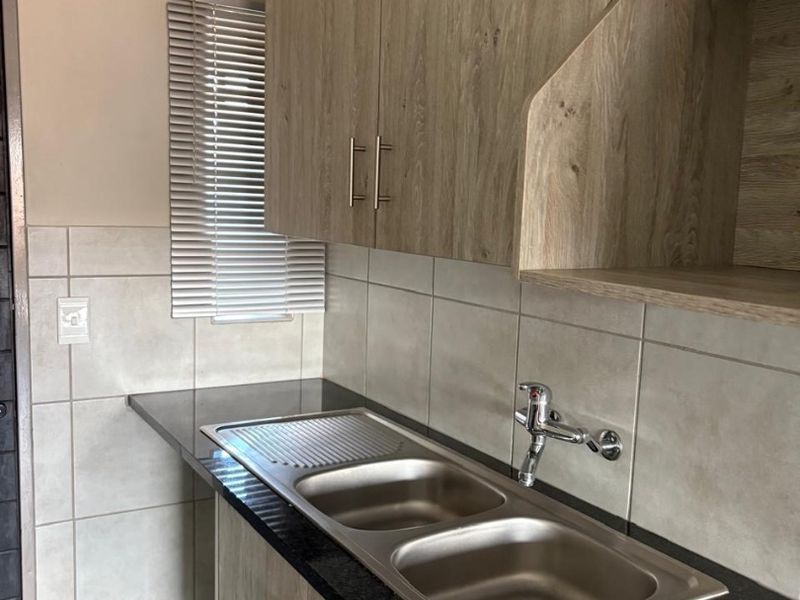 A clean and functional kitchen area featuring modern wood-look cabinetry, dark granite countertops, and a double stainless steel sink with tiled splashbacks.