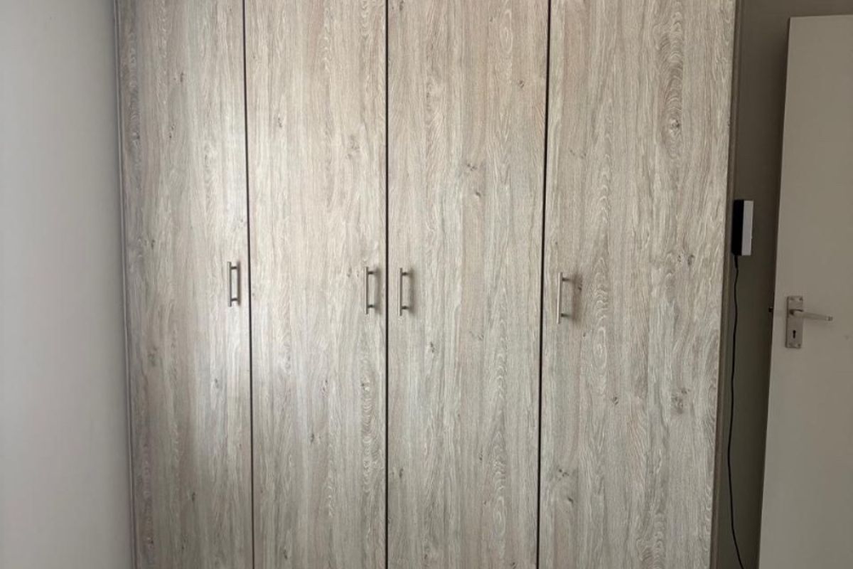 A clean bedroom featuring a large, modern wood-grain built-in wardrobe and neutral tiled flooring.
