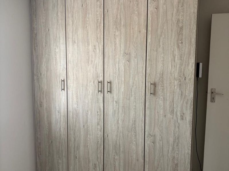 A clean bedroom featuring a large, modern wood-grain built-in wardrobe and neutral tiled flooring.