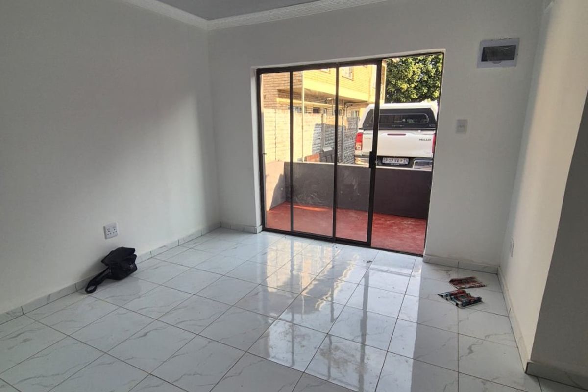A bright, empty living room featuring modern white marble-look floor tiles, coved ceilings, and a sliding glass door providing access to an outdoor area.