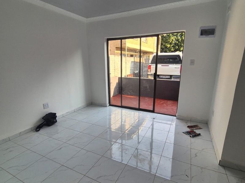 A bright, empty living room featuring modern white marble-look floor tiles, coved ceilings, and a sliding glass door providing access to an outdoor area.