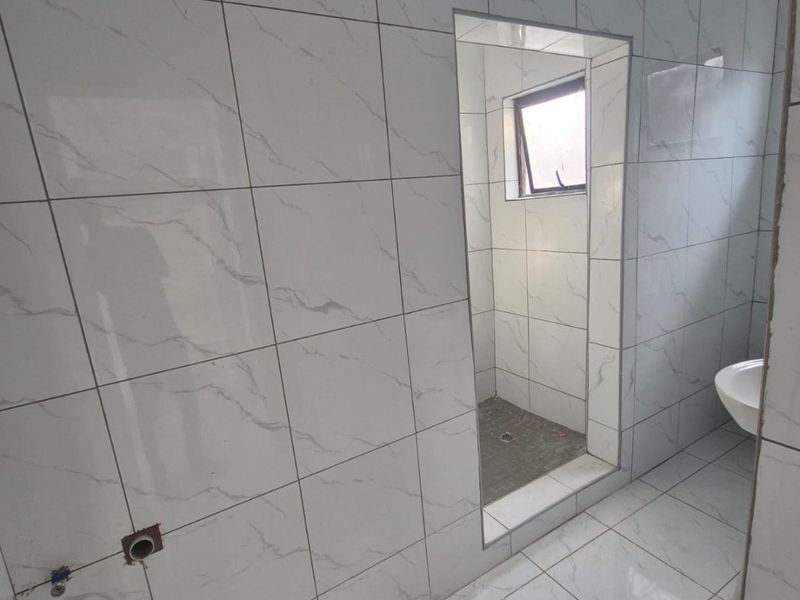 An unfinished bathroom space featuring marble-look ceramic tiling, a walk-in shower area, and exposed plumbing rough-ins awaiting final fixture installation.