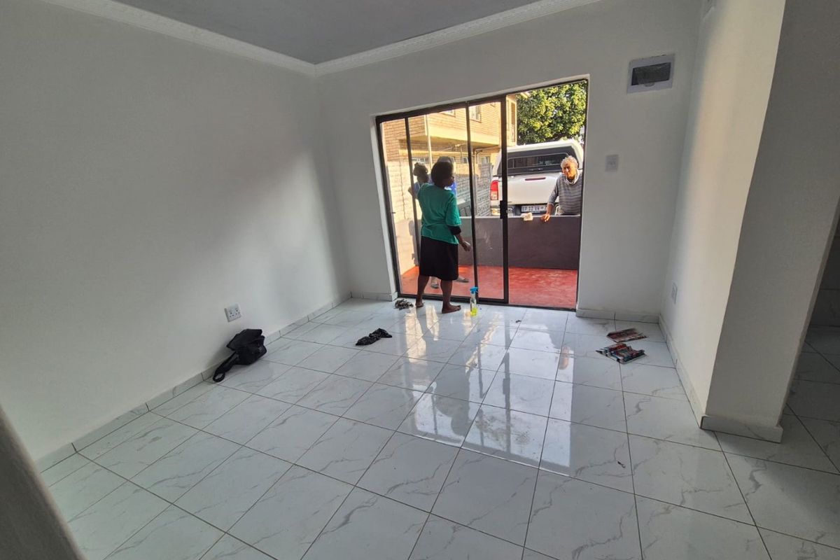 A bright, empty living room featuring modern white marble-look floor tiles, coved ceilings, and a sliding glass door leading to an outdoor patio area.