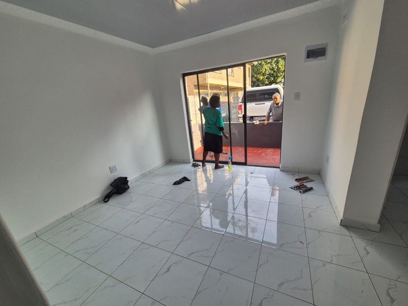 A bright, empty living room featuring modern white marble-look floor tiles, coved ceilings, and a sliding glass door leading to an outdoor patio area.