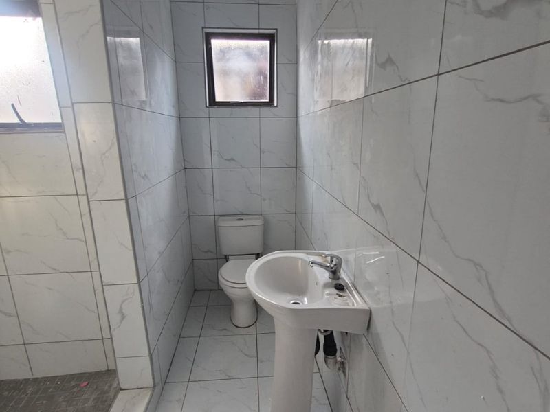 A clean, modern bathroom featuring white marble-look wall and floor tiles, a pedestal basin, toilet, and a walk-in shower area.