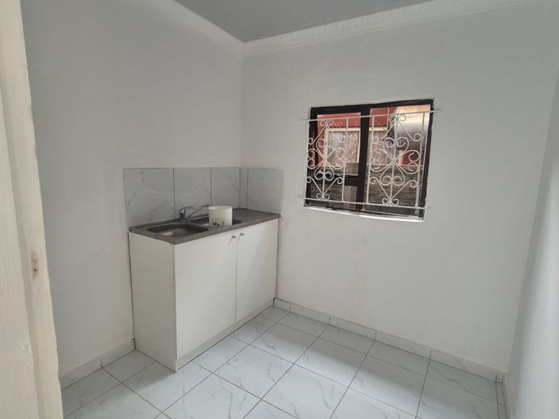 A compact, clean scullery or utility area featuring a stainless steel sink, base cabinetry, tiled splashback, and modern marble-look floor tiles.