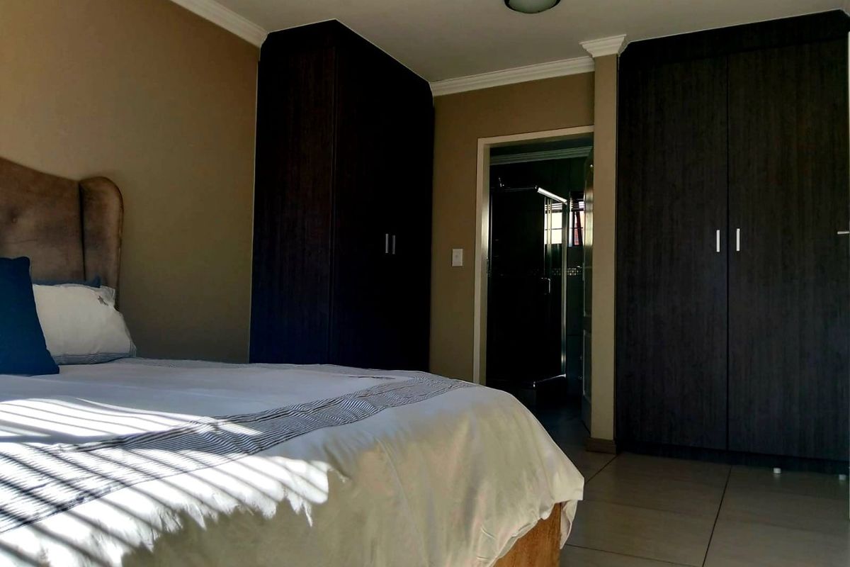 A well-maintained bedroom featuring dark wood built-in cupboards, neutral wall tones, and tiled flooring, with direct access to an en-suite bathroom.