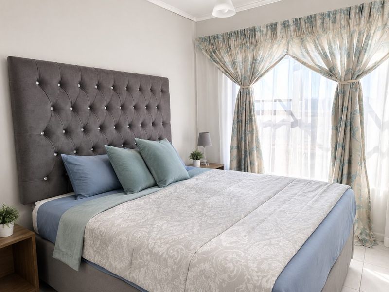 A well-maintained bedroom featuring neutral wall finishes, tiled flooring, and large windows with installed curtain tracks, providing ample natural light.
