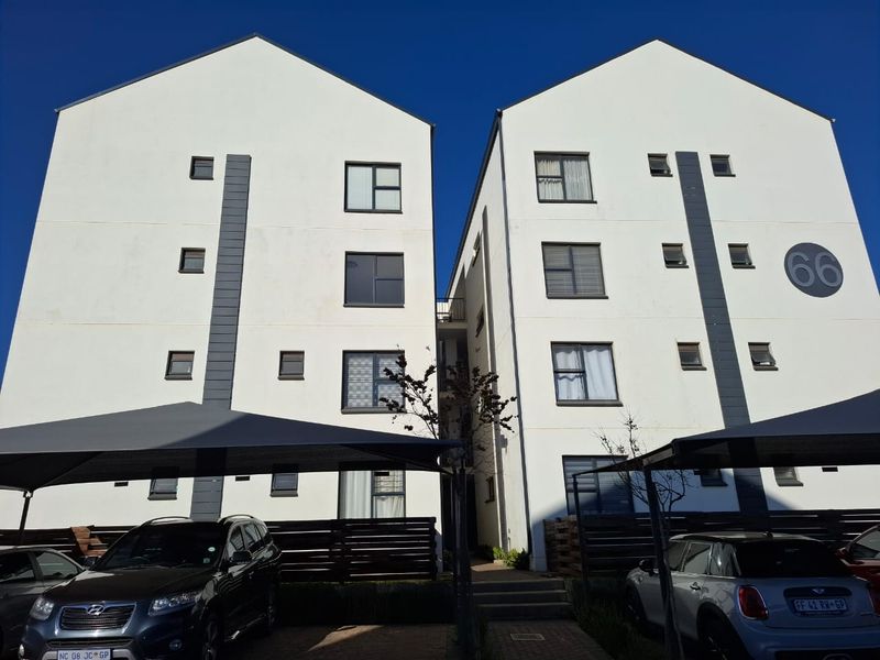 Front elevation of a modern multi-story apartment complex featuring white facades, dark accent detailing, and covered parking bays.