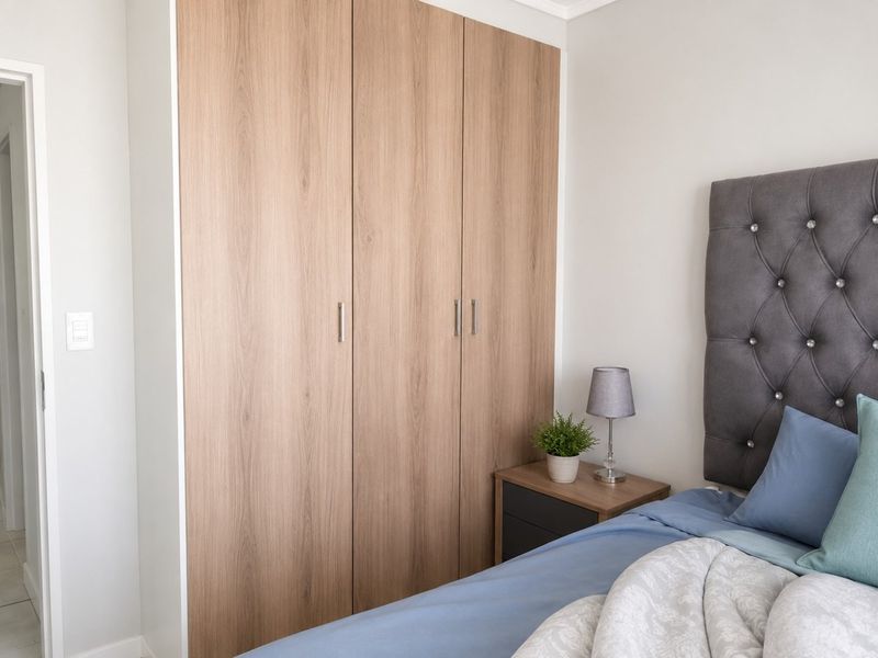 A well-maintained bedroom featuring modern, light wood-finish built-in wardrobes with clean lines and neutral wall finishes.