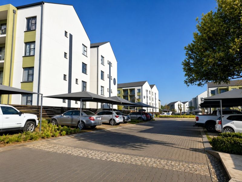 Exterior view of a modern apartment complex featuring paved parking areas with shade cloth carports and well-maintained building facades.