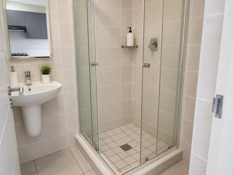 A clean and modern bathroom featuring a pedestal basin, chrome fixtures, and a glass-enclosed shower with neutral ceramic tiling.