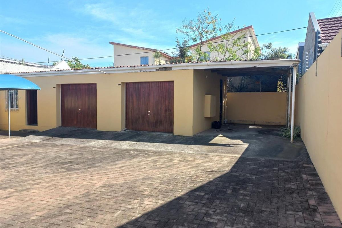 A paved driveway leading to a double garage with an attached carport, featuring a boundary wall and exterior lighting.