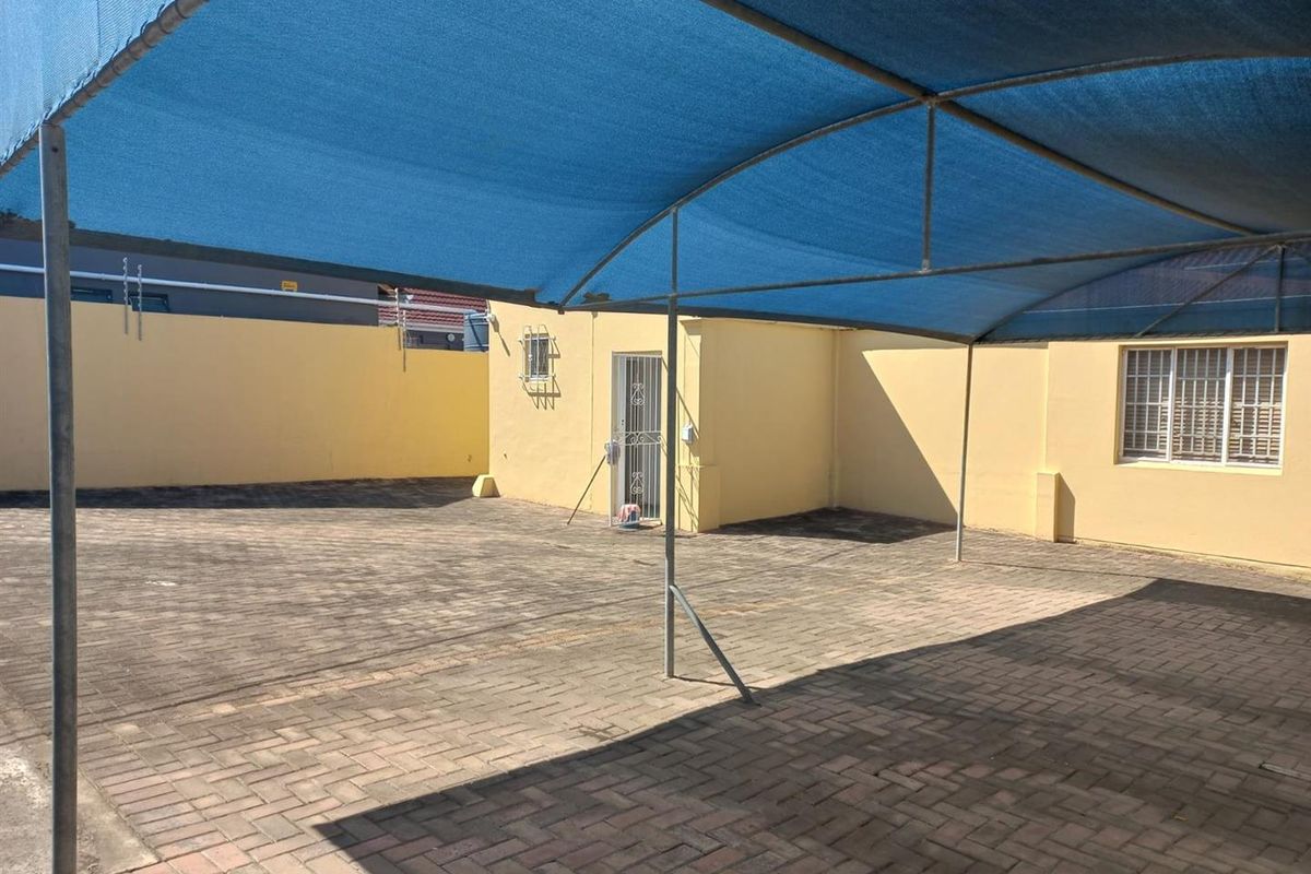A paved rear courtyard area featuring a large blue shade cloth canopy, perimeter walling, and secure access points.