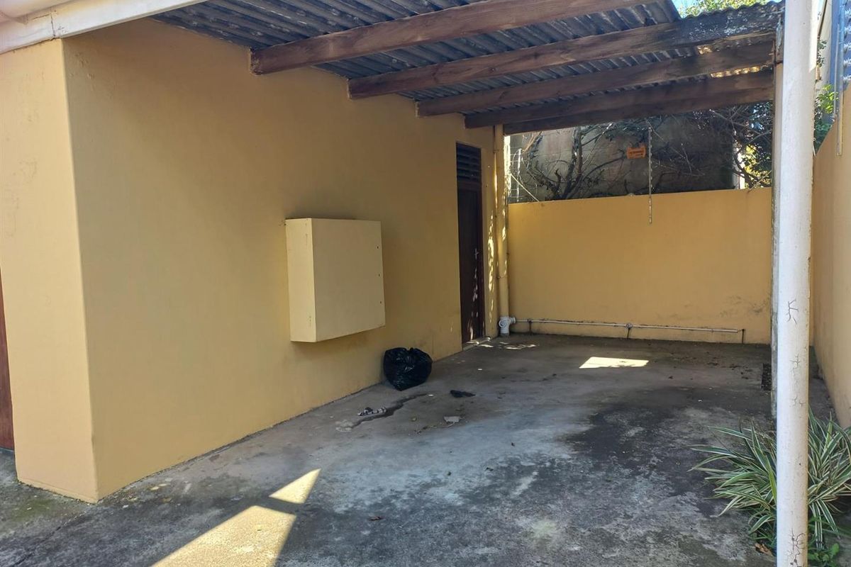 A covered outdoor patio area featuring a corrugated metal roof, timber rafters, and concrete flooring, suitable for renovation or outdoor living space enhancement.