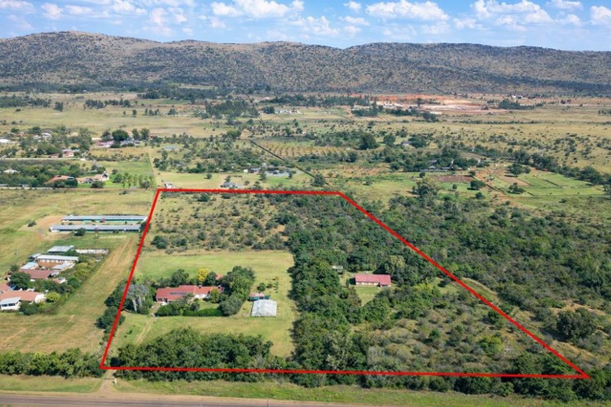 Aerial view of a large farm property featuring a main residence, secondary building, and expansive open land with mountain views in the background.