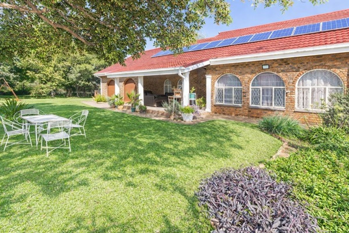 Rear view of a brick farmhouse featuring a covered patio, arched windows, and a roof-mounted solar panel system overlooking a well-maintained garden.