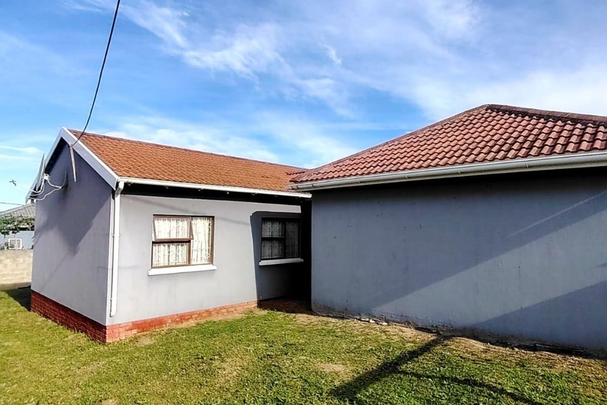Rear view of the house featuring a tiled roof, grey painted exterior walls, and a small garden area.
