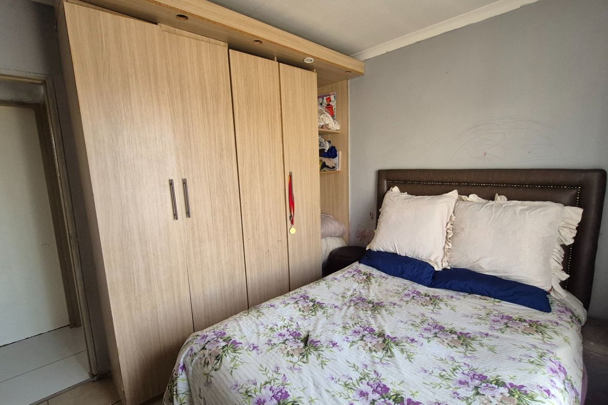 A bedroom featuring a large built-in wooden wardrobe, tiled flooring, and recessed lighting, providing functional storage space.