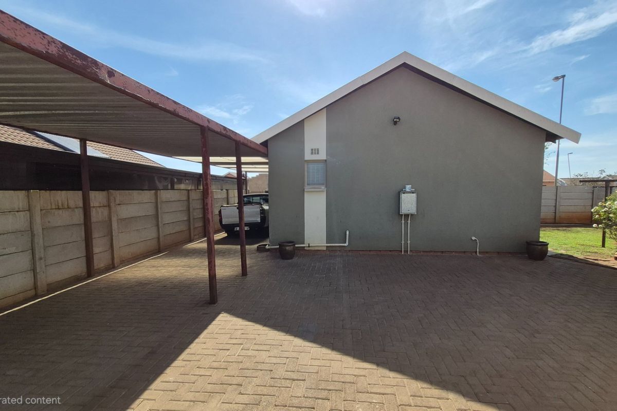 Rear exterior view featuring a paved driveway, a covered carport with metal supports, and a secure precast concrete boundary wall.